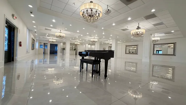 La Jolla's white hall with a grand piano and chandeliers.
