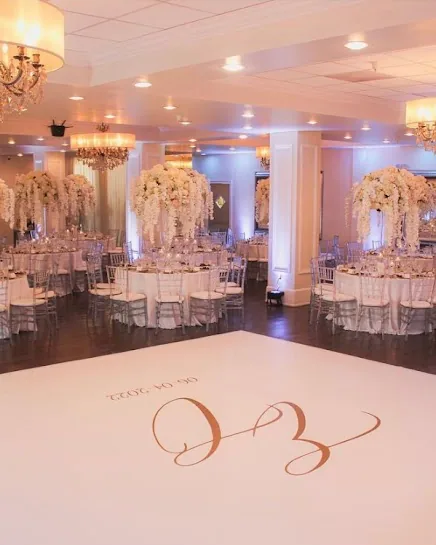 The hall in ivory light, with white orchid centerpieces and a custom monogram on the dance floor.