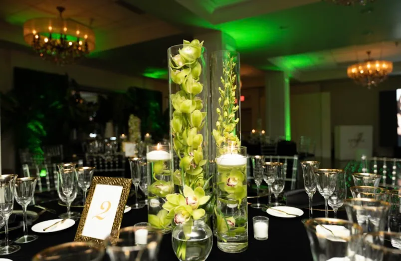 Green orchids rising in tall glass vases with floating candles on a black-dressed table under emerald light.