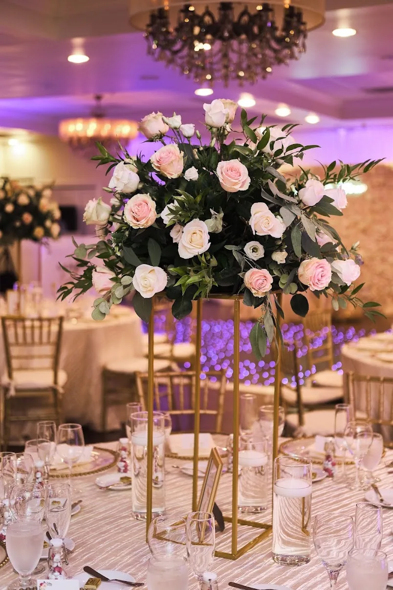 A gold stand crowned with blush and ivory roses above a table set with gold-rimmed chargers and glassware.